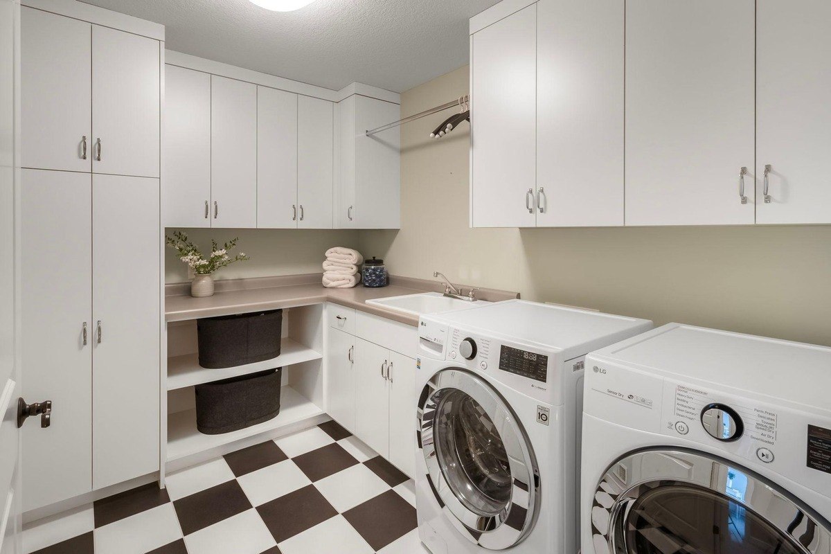 Bright and airy laundry room with white cabinetry, a checkerboard tile floor, and ample storage space offers a functional and stylish space for household chores.