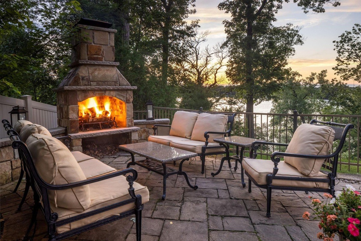 Outdoor seating area with a stone fireplace, comfortable furniture, and a view of the lake creates a perfect spot for enjoying a relaxing evening.