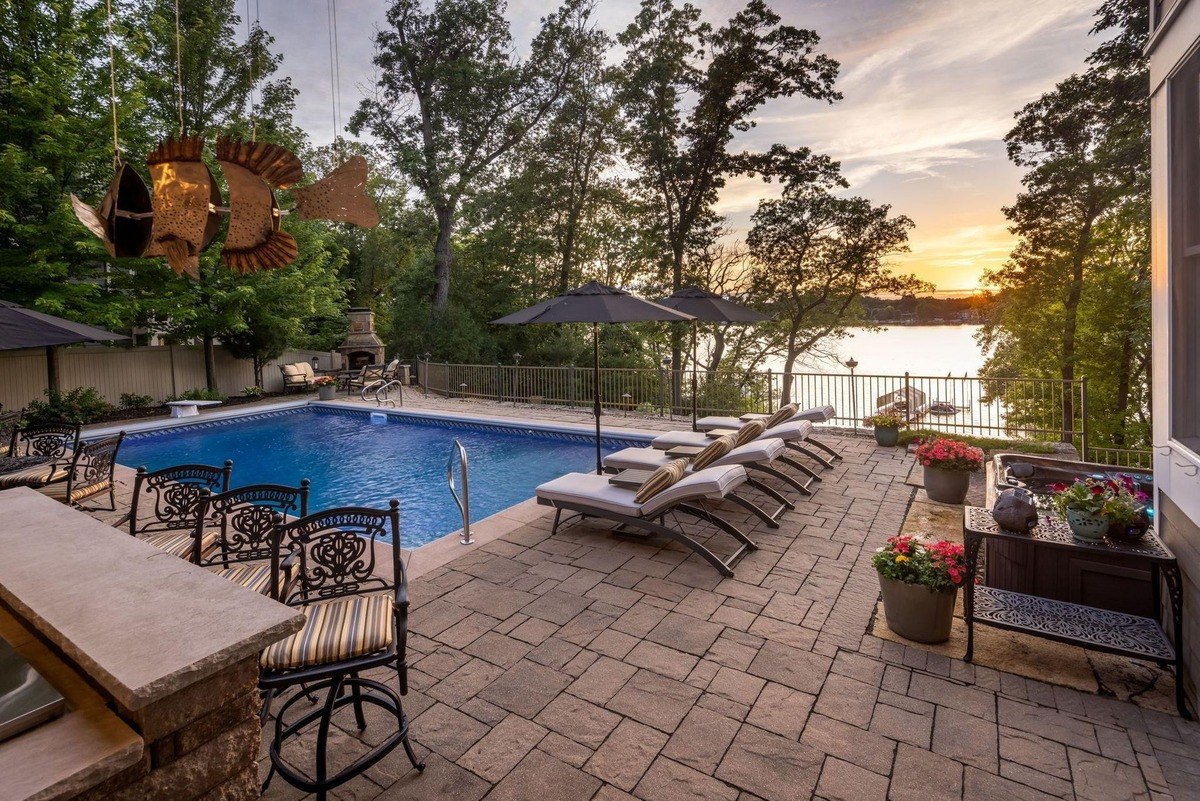 Sparkling pool surrounded by lounge chairs and a bar area offers a luxurious outdoor retreat with stunning sunset views over the lake.