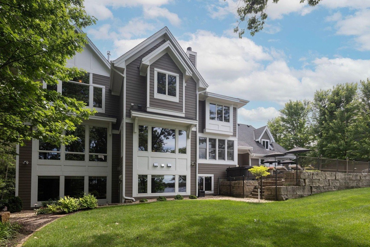 Modern home with a blend of siding and large windows sits on a landscaped lot, showcasing a well-maintained lawn and a hint of outdoor living space.