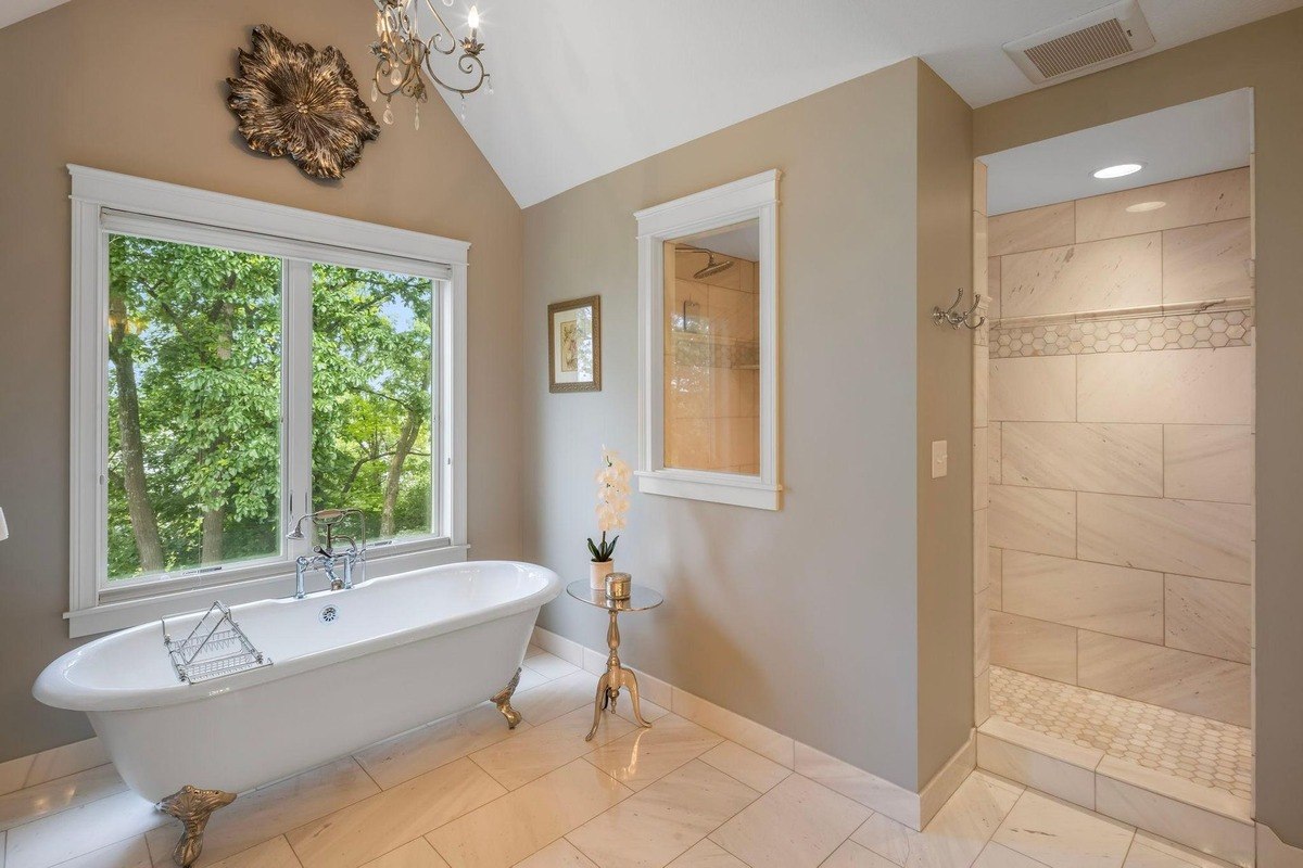 Luxurious bathroom featuring a clawfoot tub, walk-in shower, and tree-lined views.