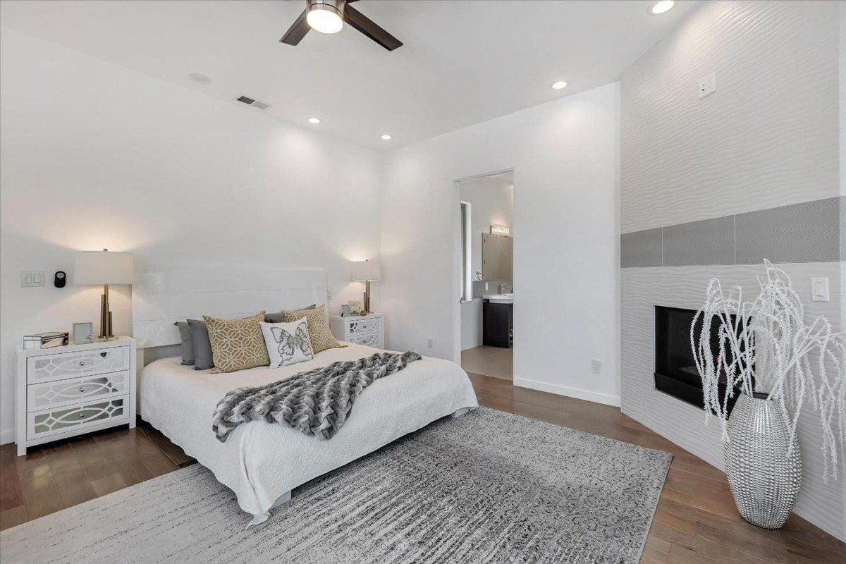 Bedroom view a modern bedroom with neutral tones, a ceiling fan, and a wall-mounted fireplace.