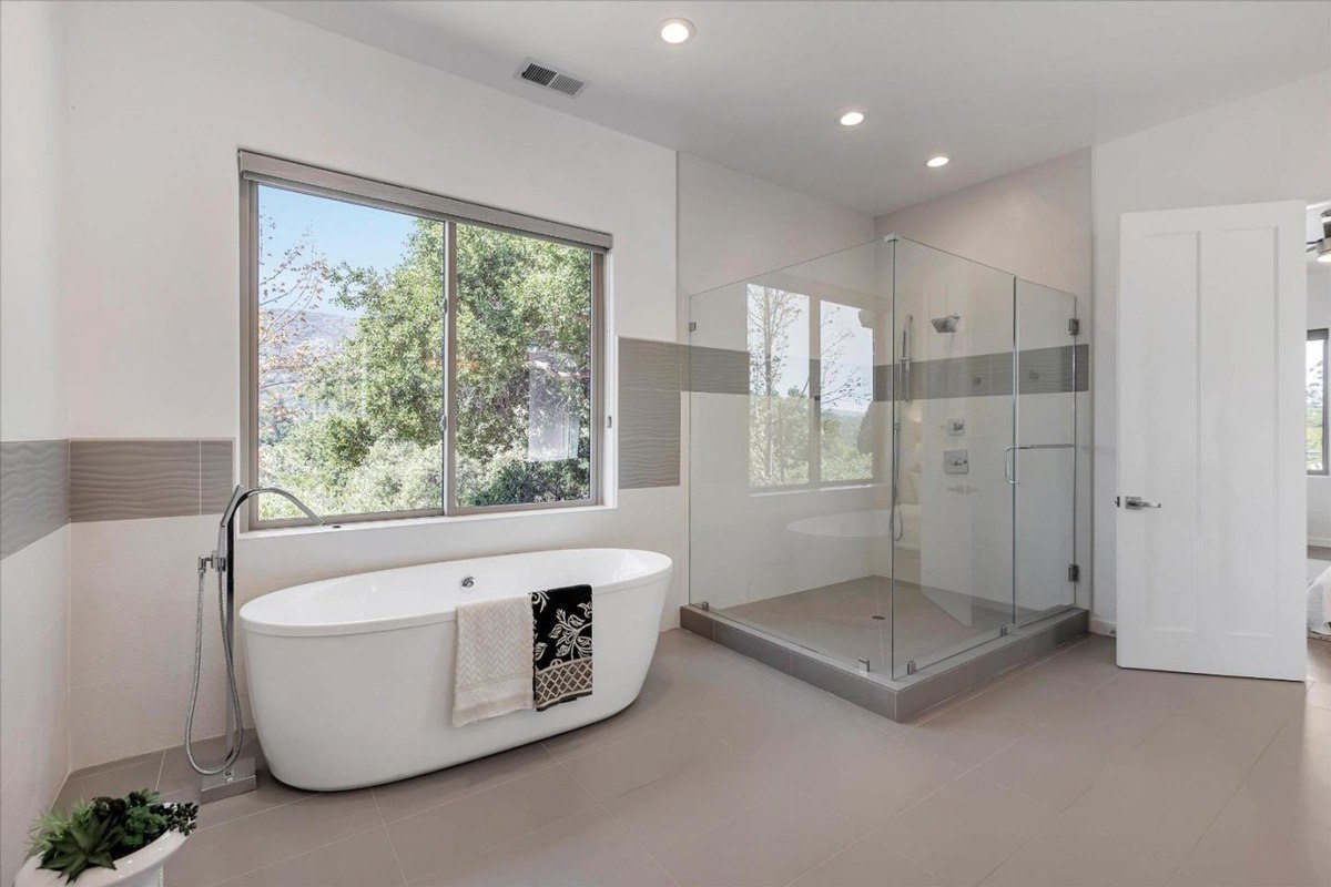 Bathtub and shower a bathroom featuring a freestanding tub, glass-enclosed shower, and large window.