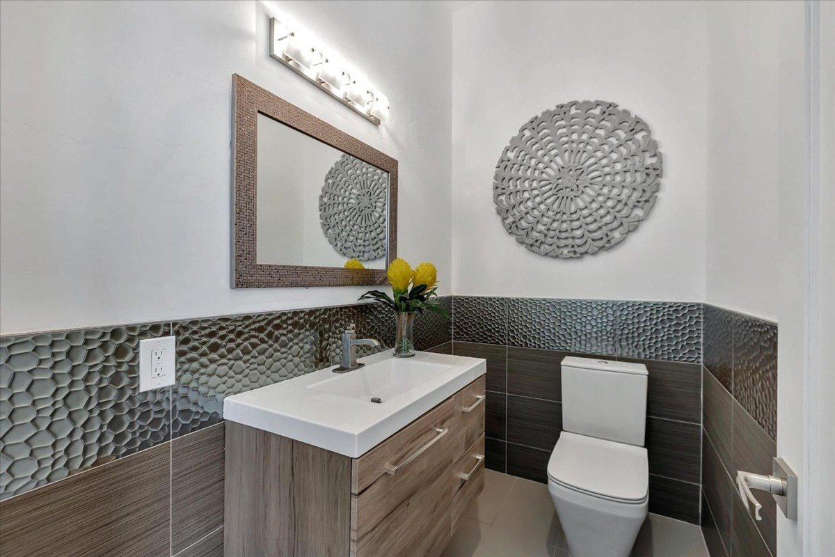 Powder room a half-bath with a decorative mirror, modern vanity, and textured wall tiles.