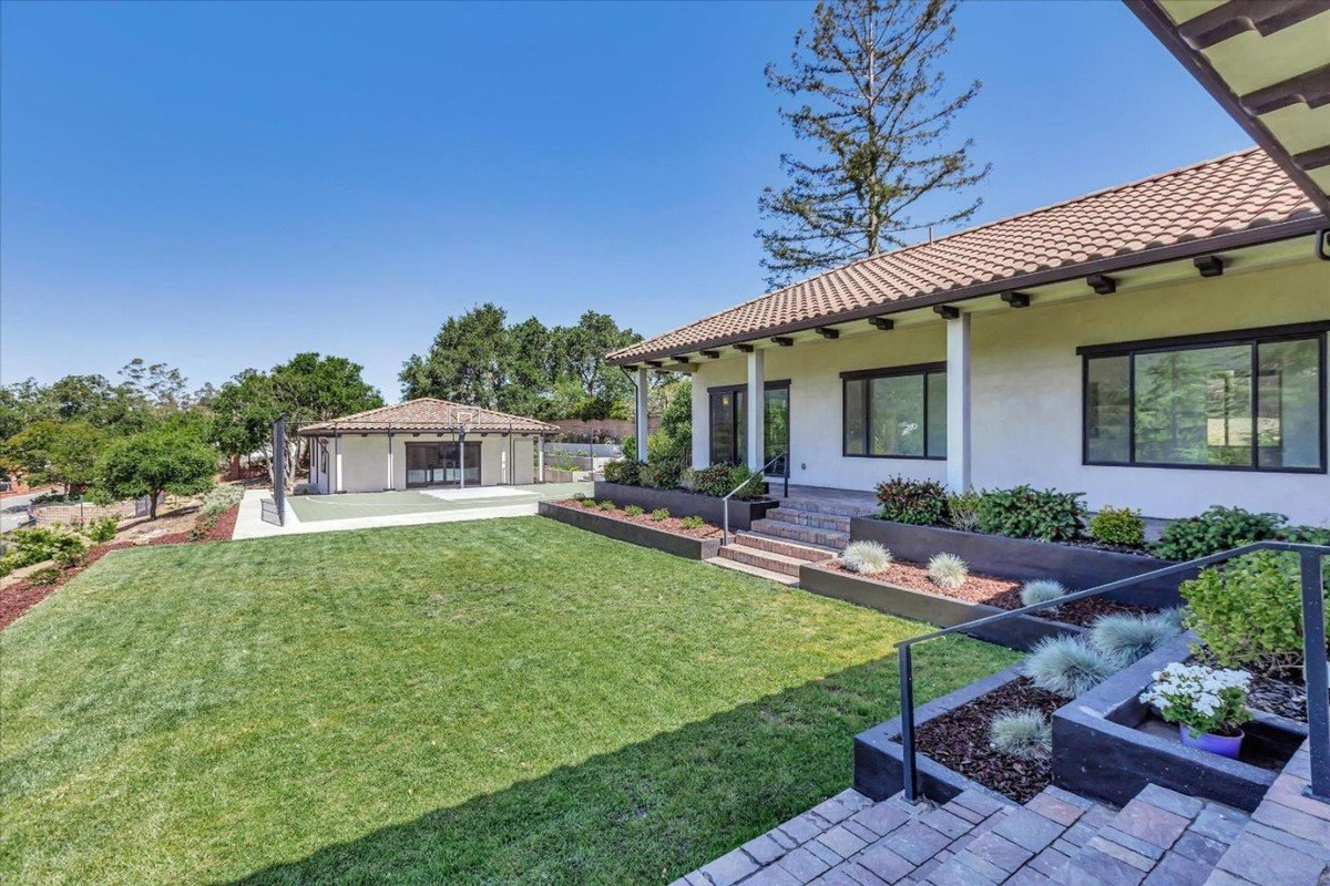 Backyard with landscaped lawn, garden beds, and a basketball court.