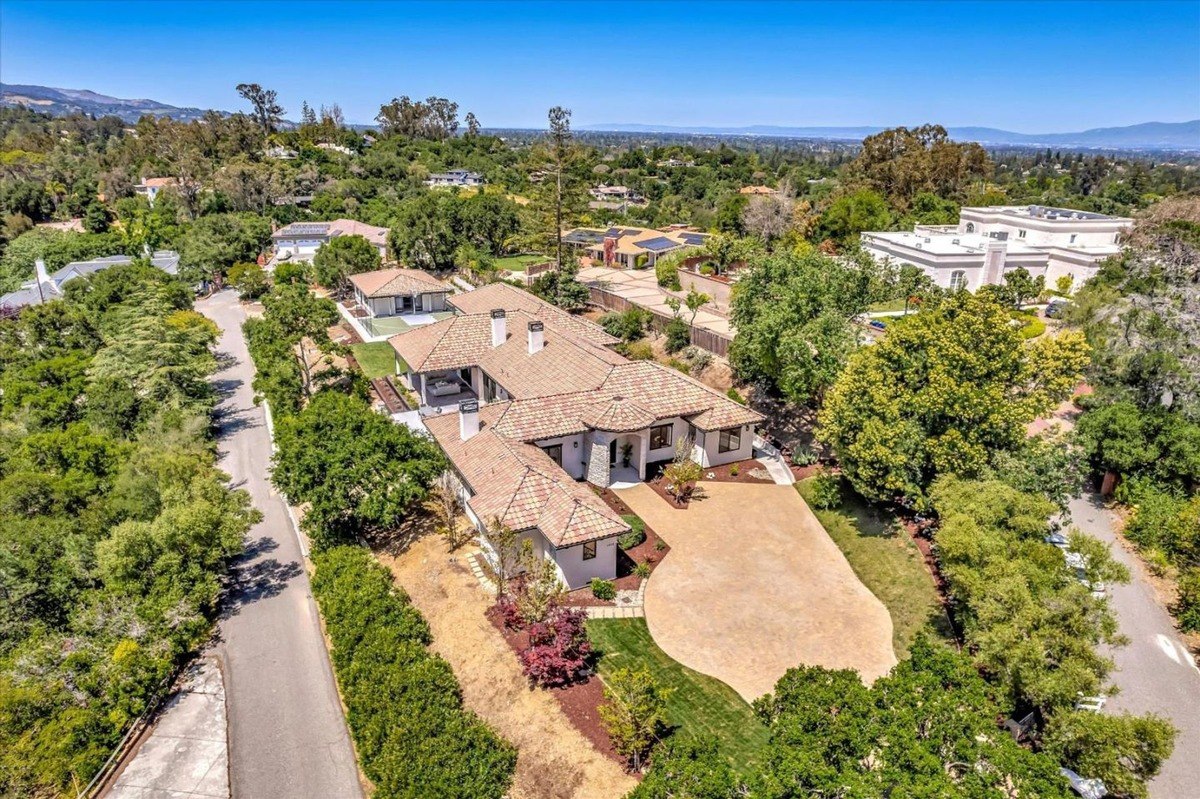 Aerial view of a luxury home with a spacious driveway, landscaped grounds, and a surrounding neighborhood of upscale properties.