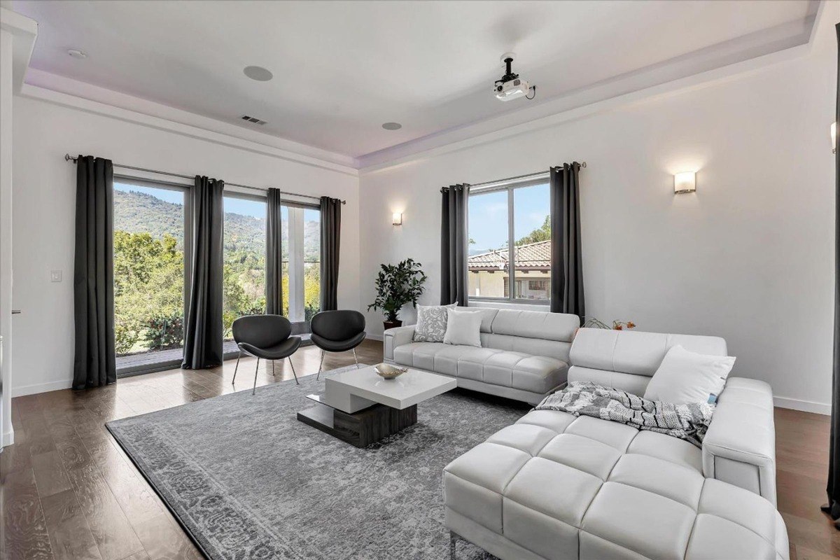 Media room with a sectional sofa, large windows, and a projector setup.