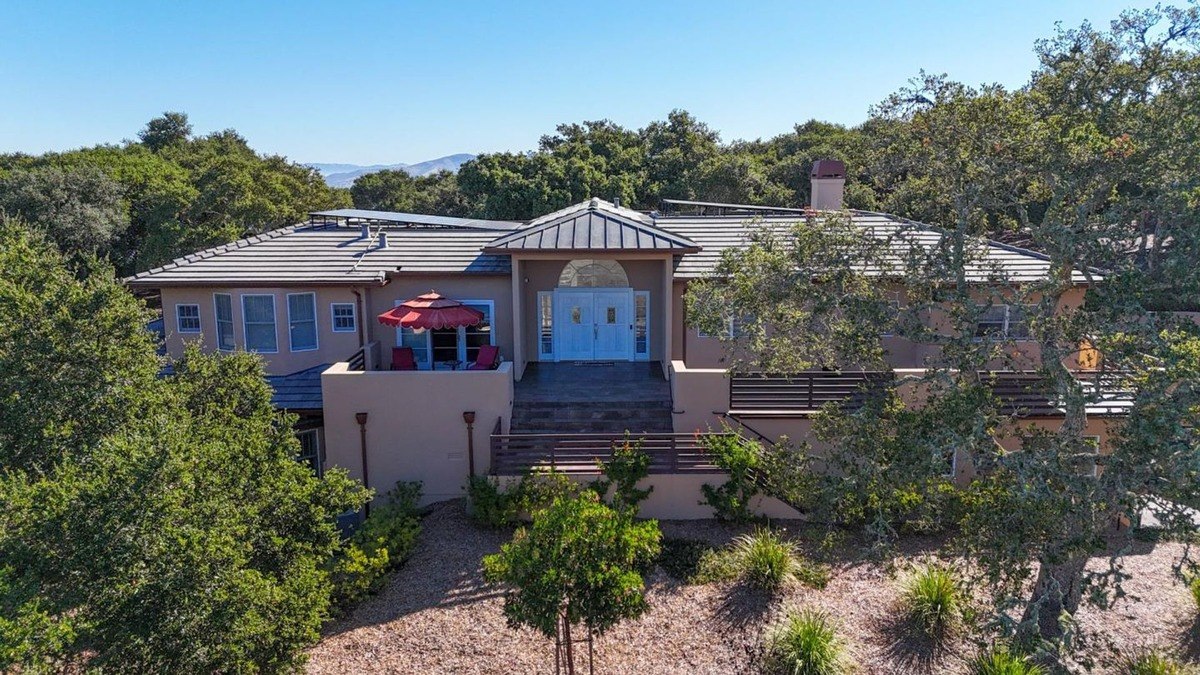 Contemporary residence with a warm stucco exterior, a metal roof, and multiple levels, nestled amidst a lush landscape with mature trees.