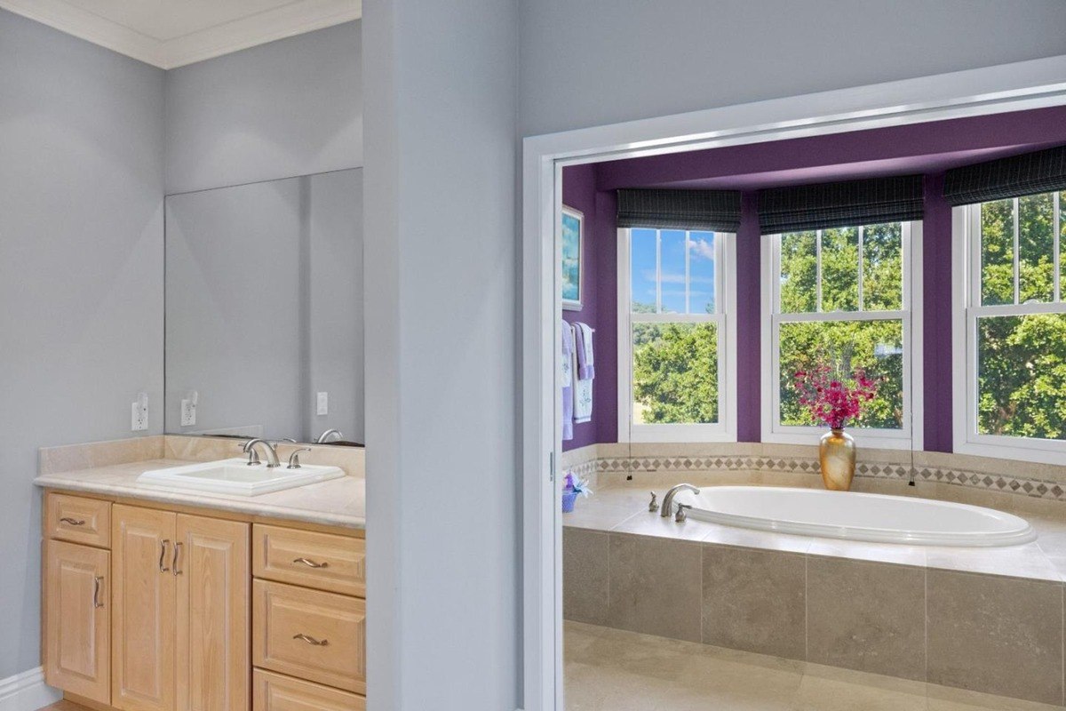 Luxurious ensuite bathroom featuring a double vanity, a freestanding bathtub with a view, and a color palette of soothing neutrals and rich purple accents.