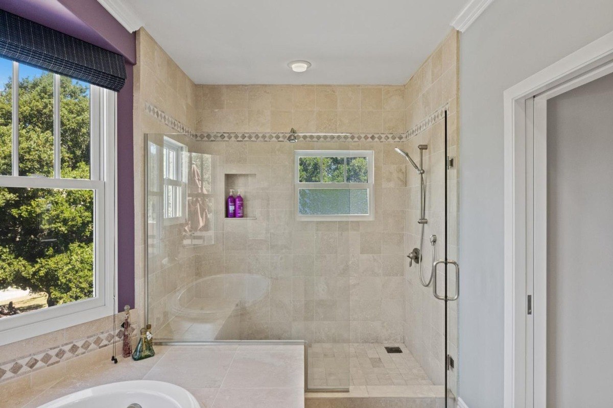 Spa-like bathroom showcasing a walk-in shower with a bench seat, a window for natural light, and elegant tilework.