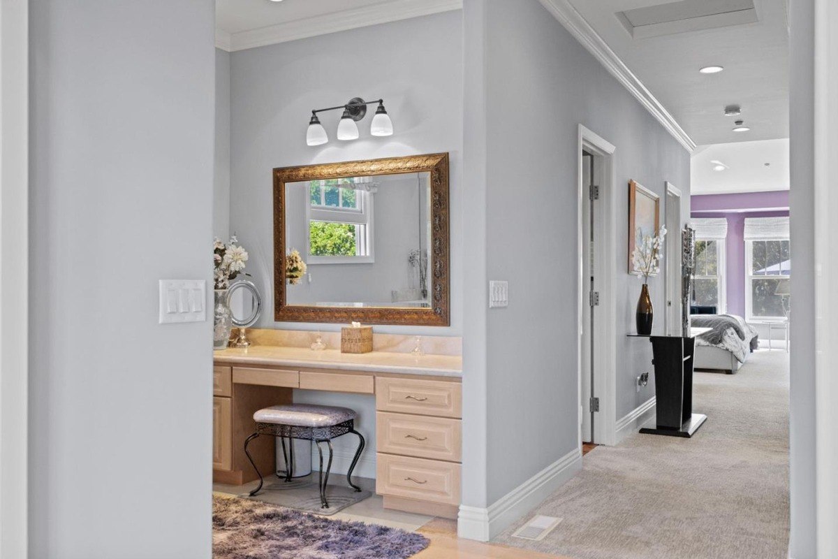 Dressing area with a vanity mirror, a stool, and ample storage, leading to a spacious bedroom with a king-sized bed.