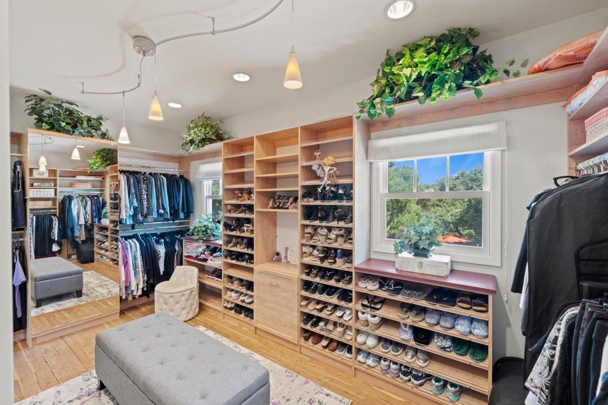 Walk-in closet with abundant shelving, a mirrored wall, and a seating area, providing ample storage for clothing and accessories.