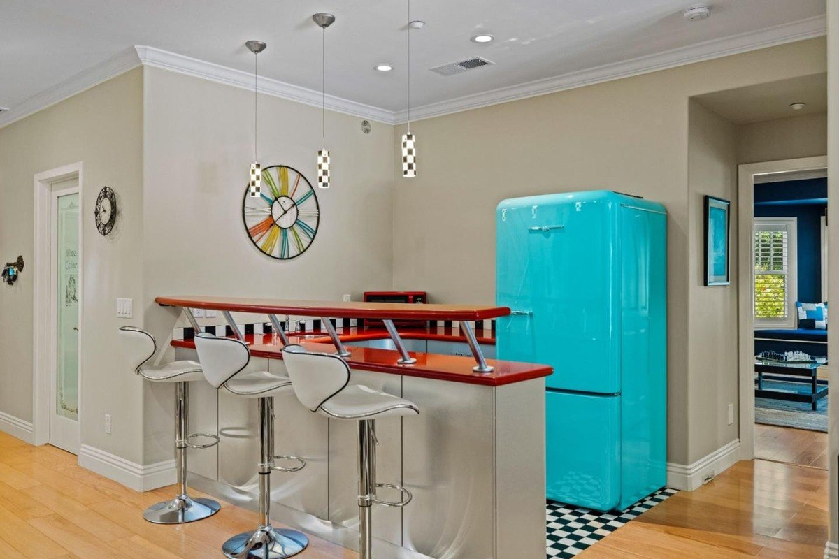 Retro-inspired kitchen nook featuring a vibrant turquoise refrigerator, a breakfast bar with sleek bar stools, and a playful clock on the wall.