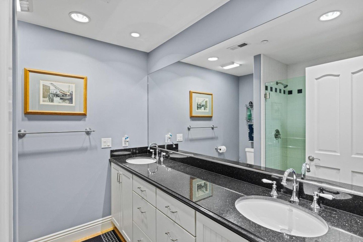 Contemporary bathroom featuring a double vanity with a black granite countertop, a large mirror, and a walk-in shower with a glass enclosure.