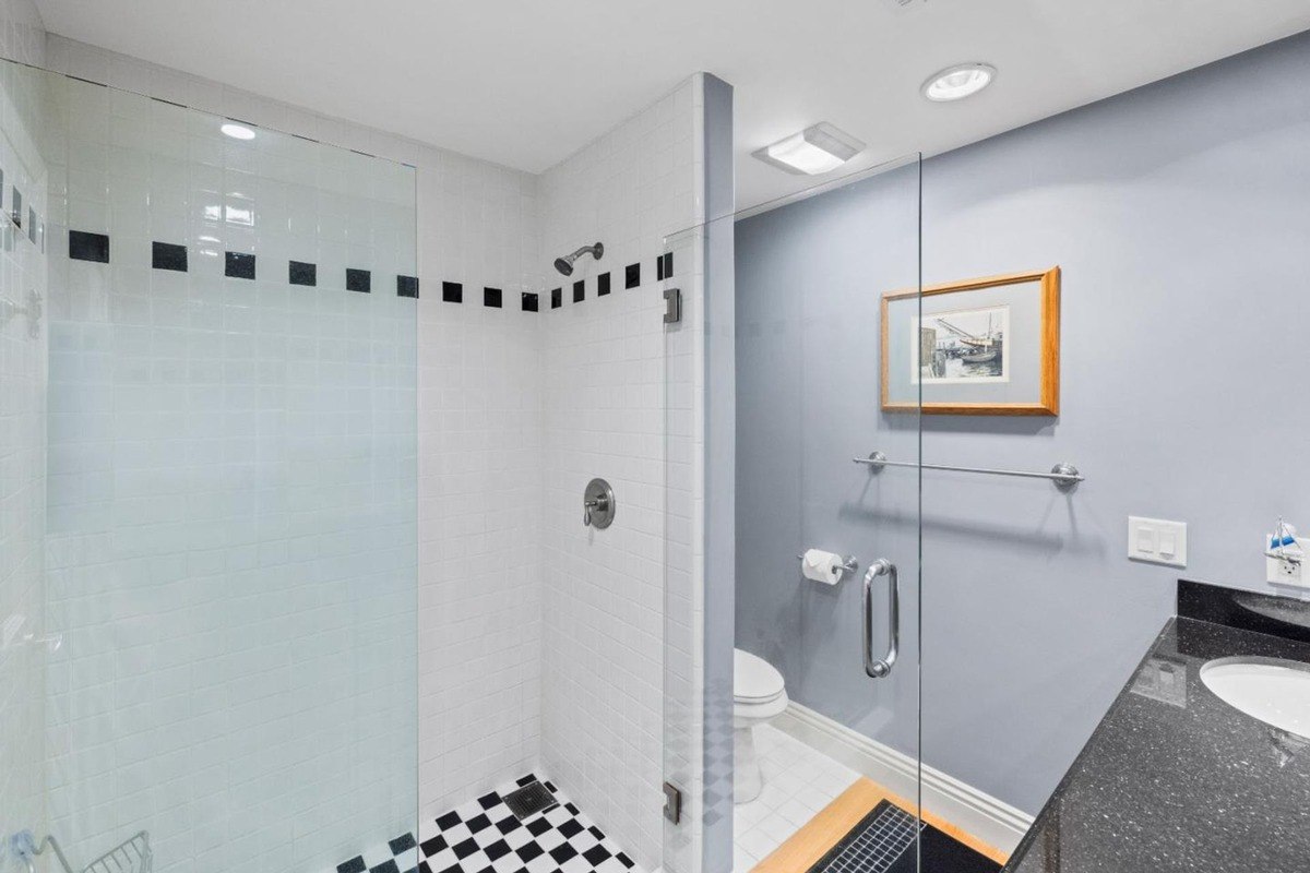 Modern bathroom with a glass-enclosed shower featuring a black and white tiled floor, a separate toilet area, and a vanity with a black granite countertop.