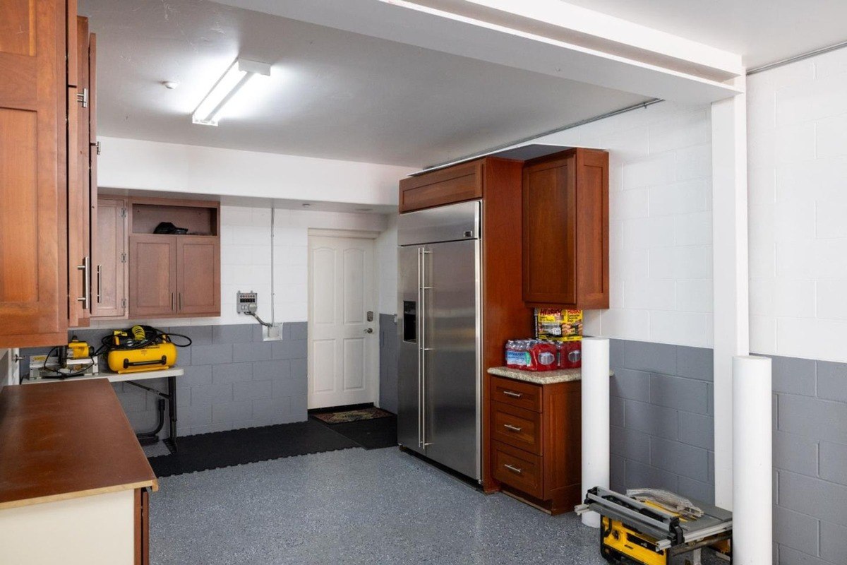 Well-organized garage space featuring built-in cabinetry, a refrigerator, and a work bench, showcasing a practical and functional design.