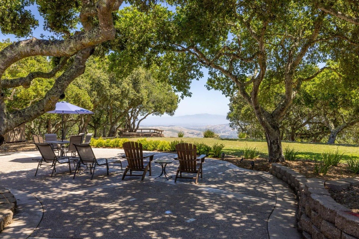 Outdoor patio nestled beneath the shade of mature oak trees, offering a tranquil seating area with a distant mountain vista.