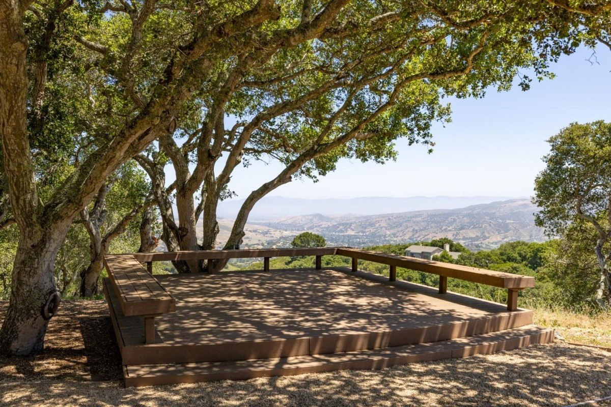 Secluded outdoor deck nestled amongst mature trees, offering a breathtaking vista of rolling hills and a distant horizon.