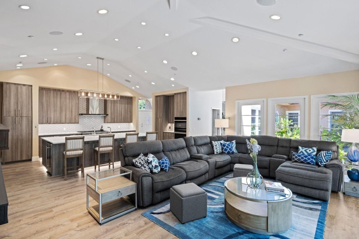 Open-concept living space seamlessly integrates a modern kitchen with a cozy seating area, featuring a vaulted ceiling, hardwood flooring, and a neutral color palette.