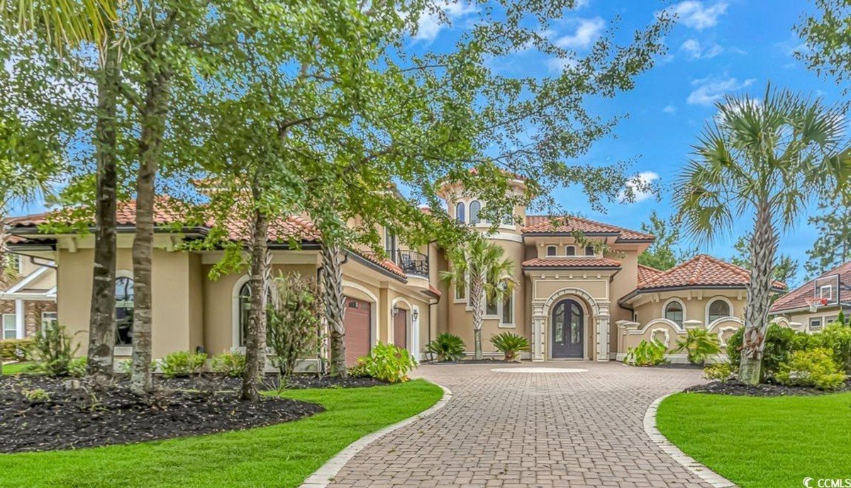 Expansive tan residence featuring a sophisticated brick driveway.