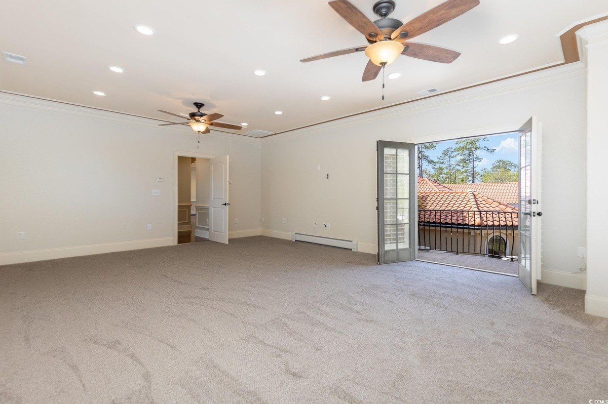 Room has carpeting, two ceiling fans, and French doors leading to a balcony.