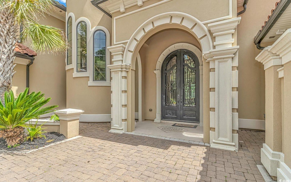 House entrance has arched entryway, double doors, and brick pavers.