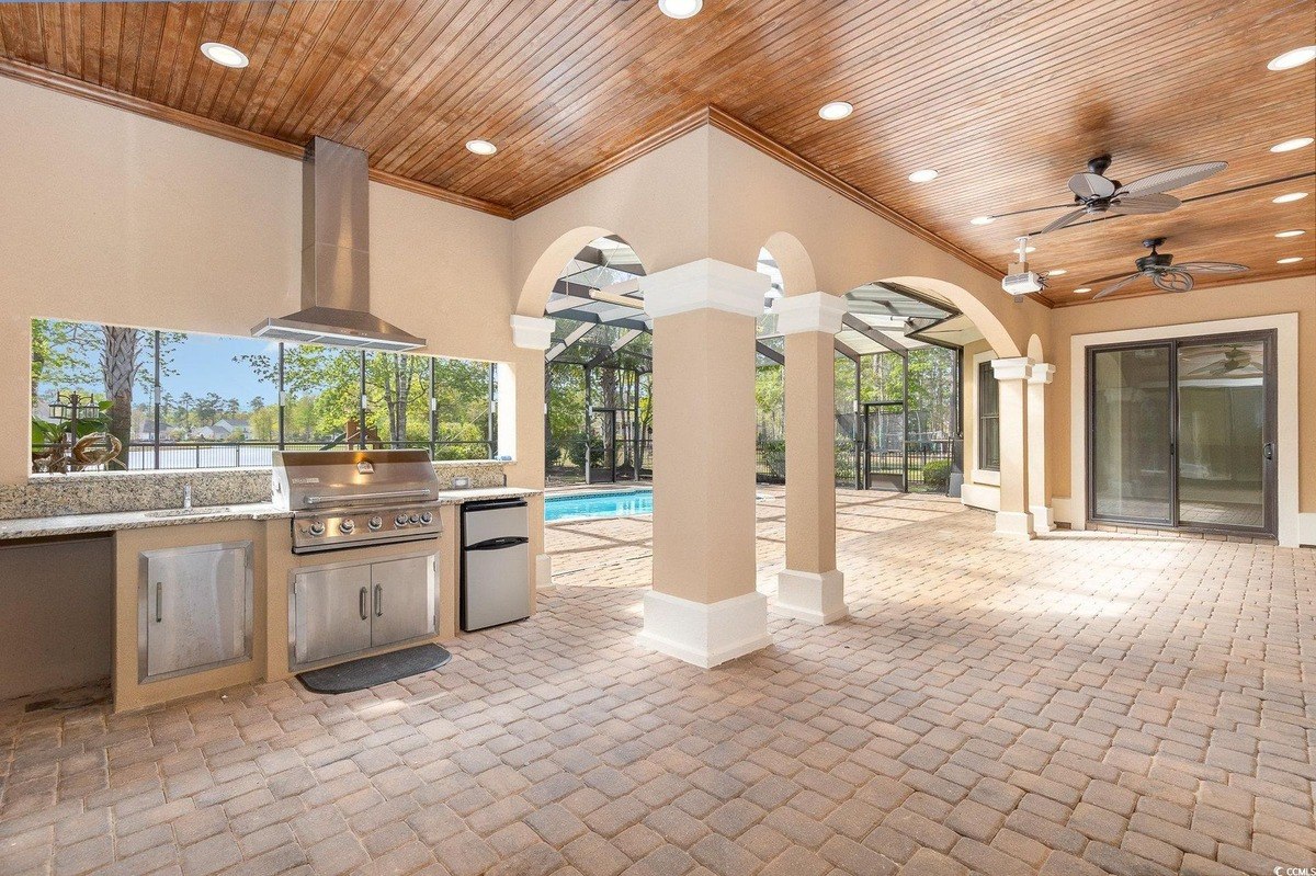 Outdoor kitchen area has a built-in grill, refrigerator, and wood ceiling.