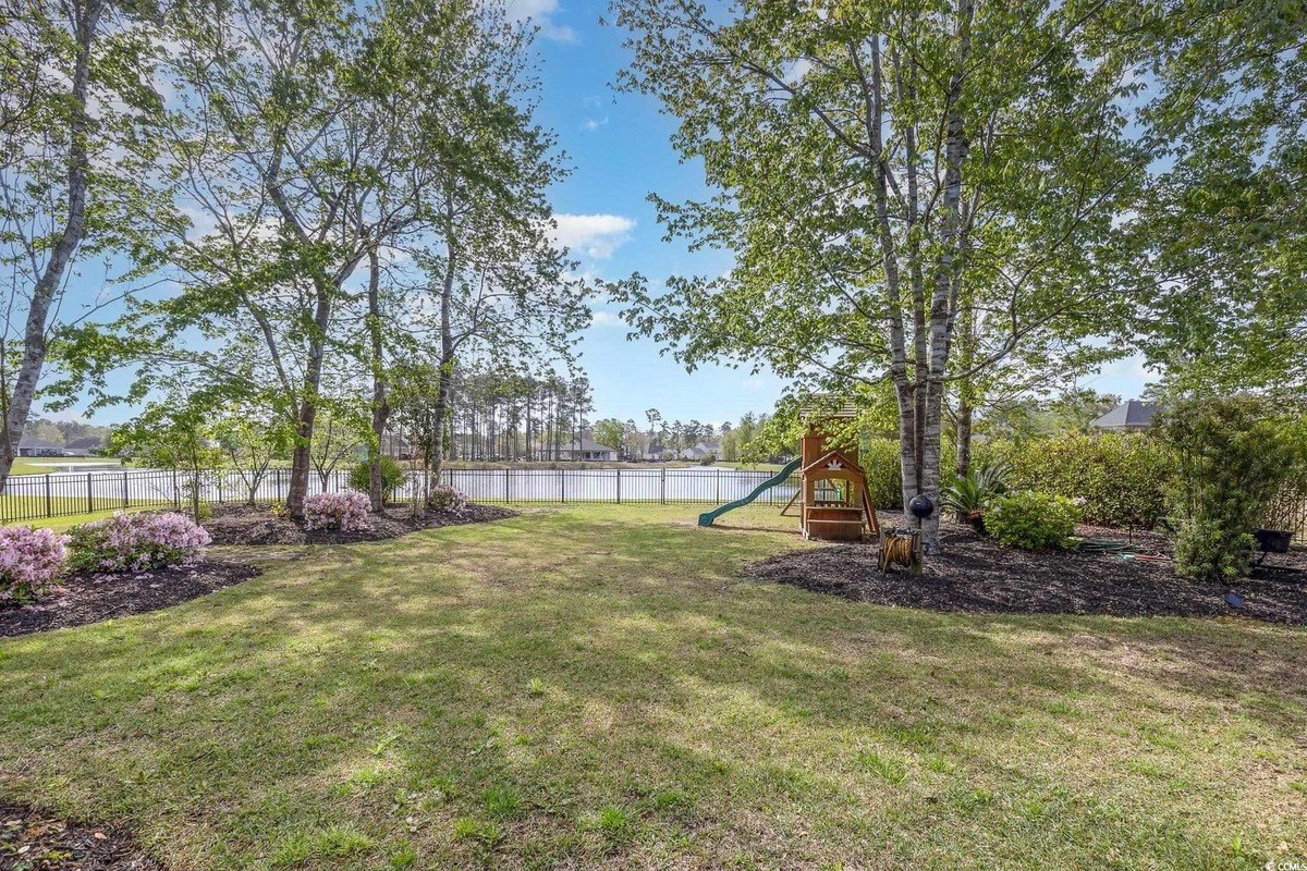 Backyard has a grassy area, trees, and a playground, overlooking a lake.