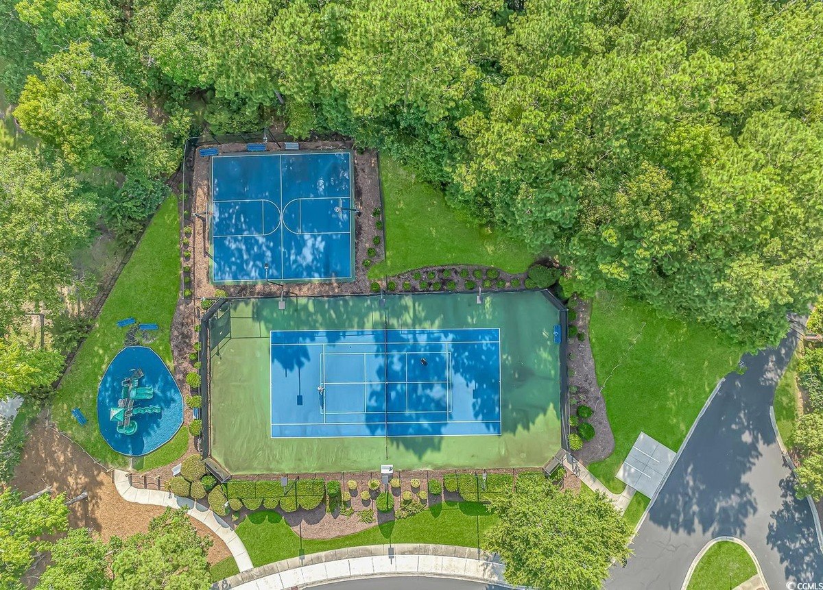 Aerial view shows tennis and basketball courts surrounded by trees and a playground.