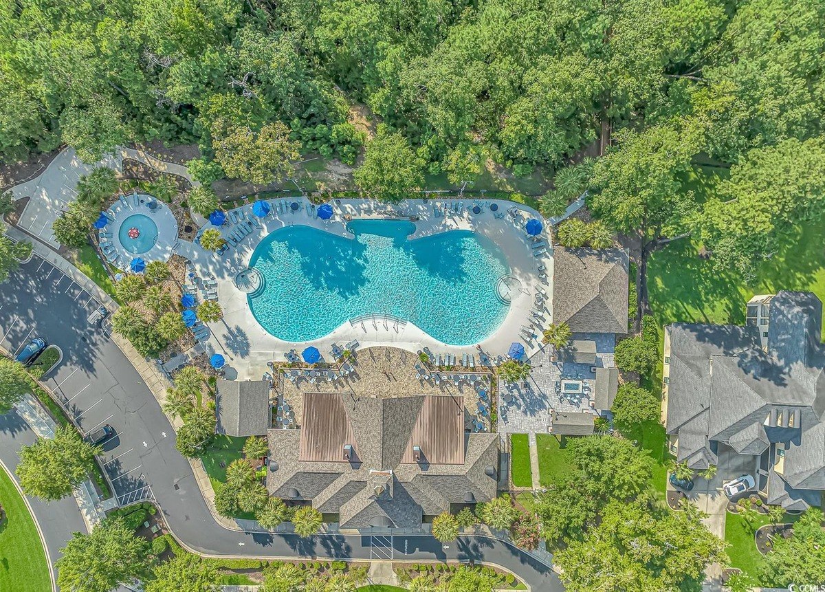 Aerial view shows a large pool, clubhouse, and surrounding trees.