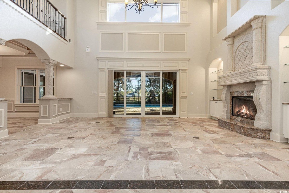 Great room has high ceilings, a fireplace, and large windows overlooking a pool.