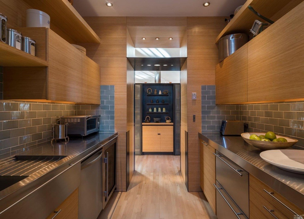 Gourmet kitchen pantry features sleek stainless steel countertops, custom wood cabinetry, and open shelving with modern lighting.