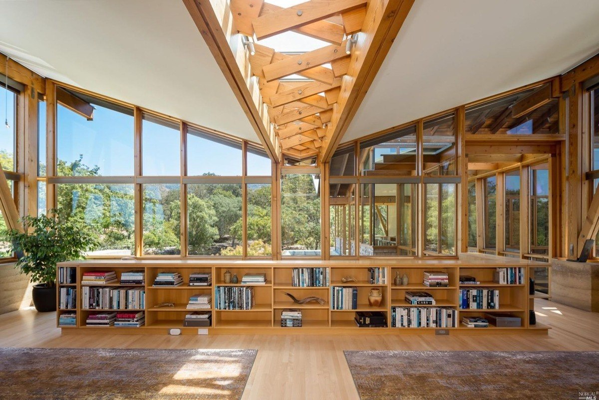 Library area showcases built-in shelves beneath expansive triangular windows and natural wood beams.