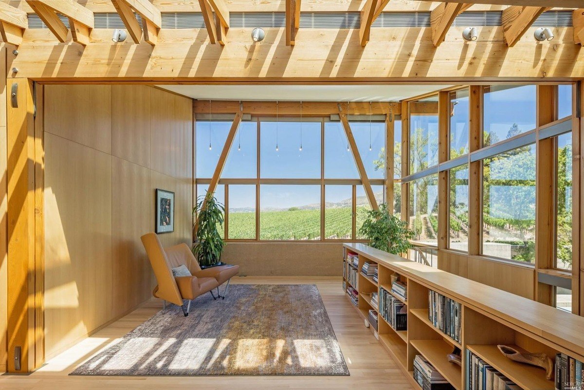 Reading corner with armchair and floor-to-ceiling glass provides panoramic vineyard scenery and natural light.