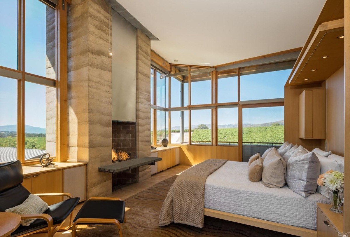 Master bedroom includes a fireplace with a stone mantle, large corner windows, and modern wood accents.