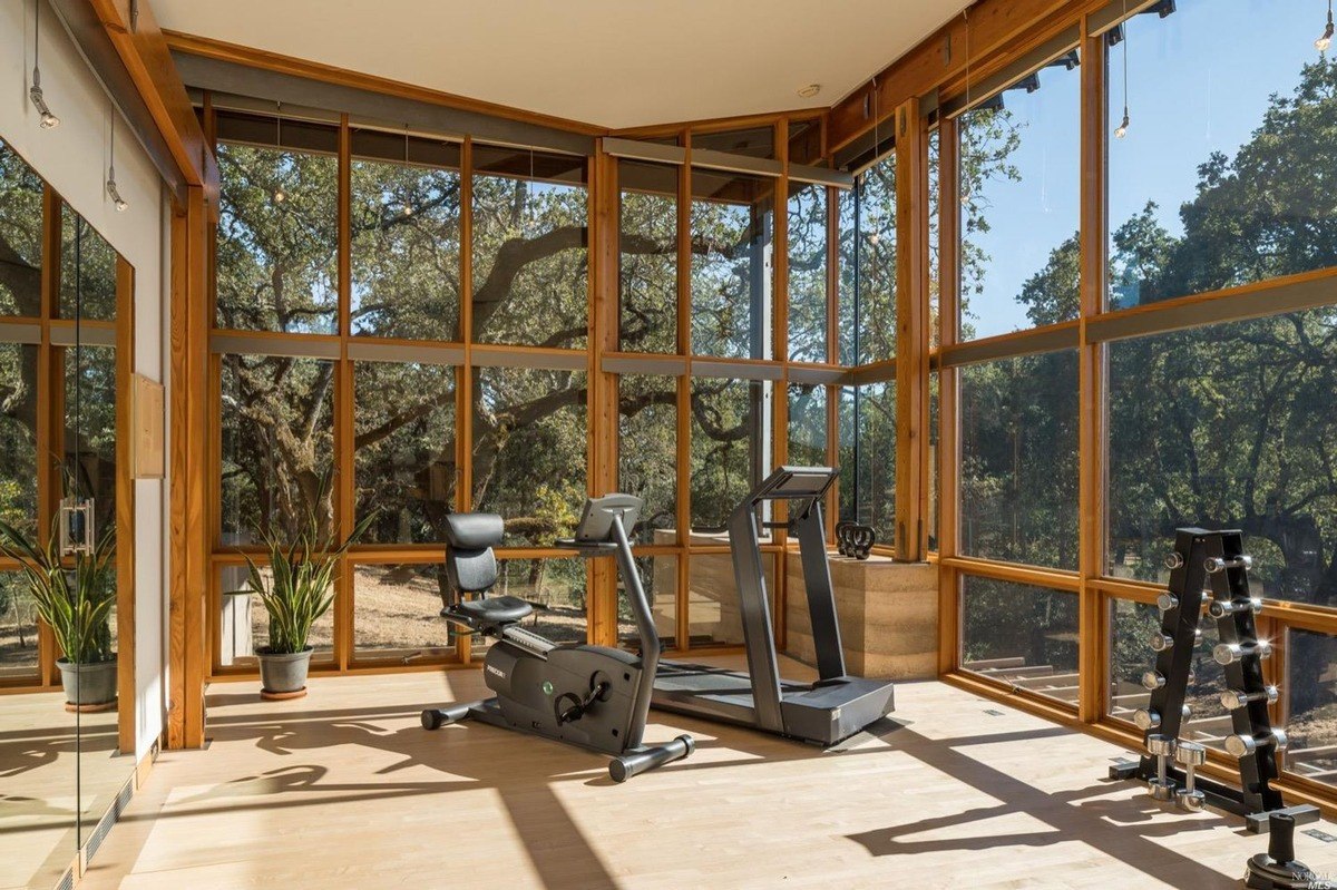 Home gym with glass walls provides an open view of the surrounding oak trees.