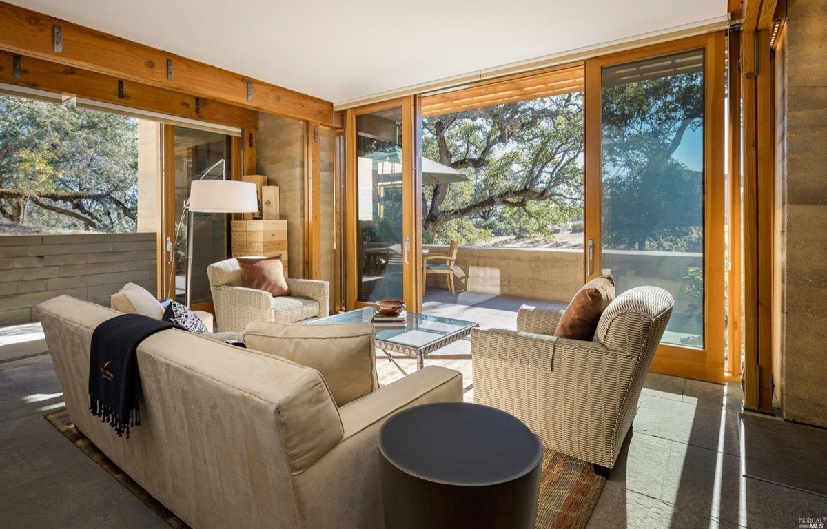 Outdoor lounge area opens to a patio through sliding glass doors with outdoor seating and forest views.