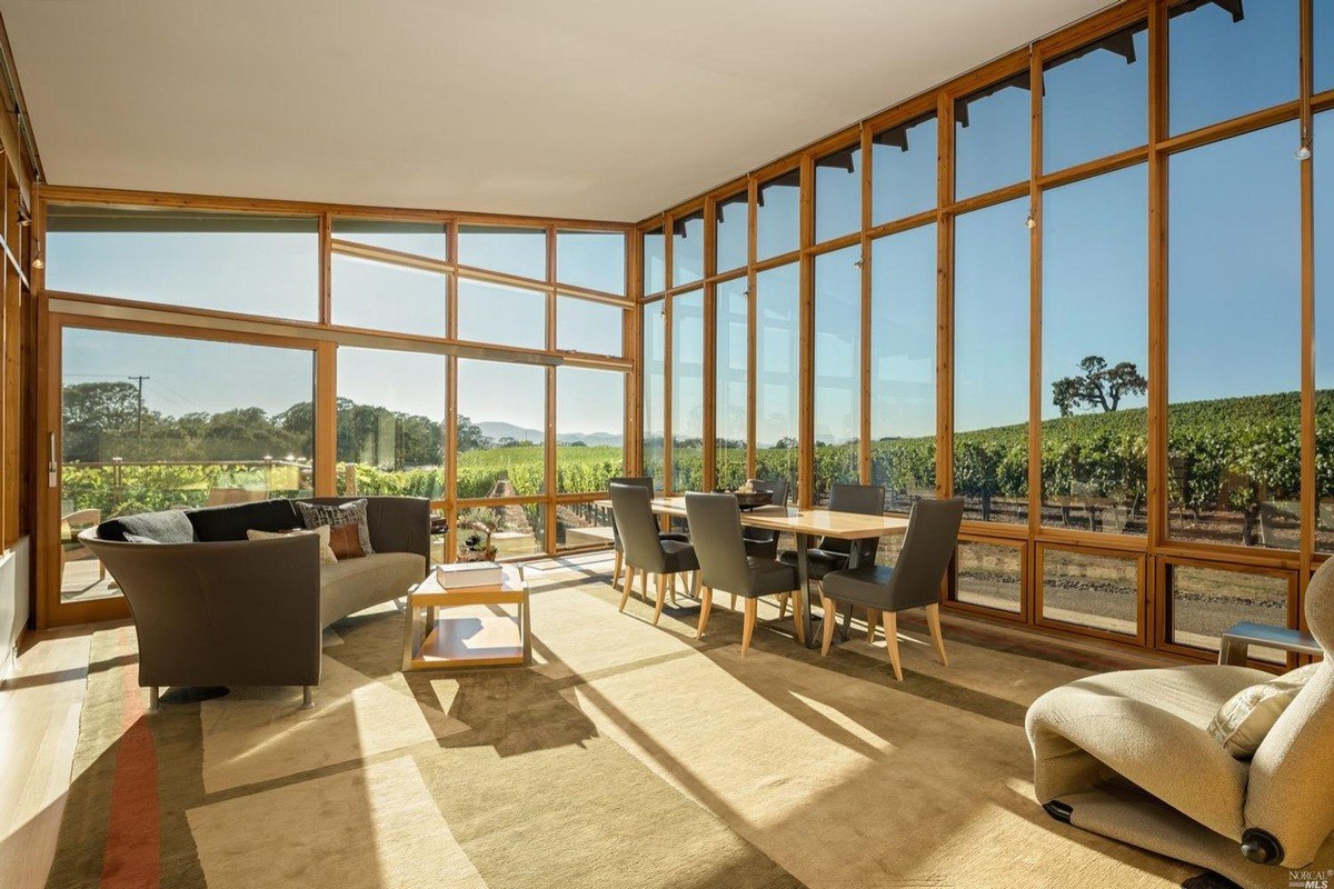 Bright sitting area surrounded by large windows offering panoramic vineyard views.