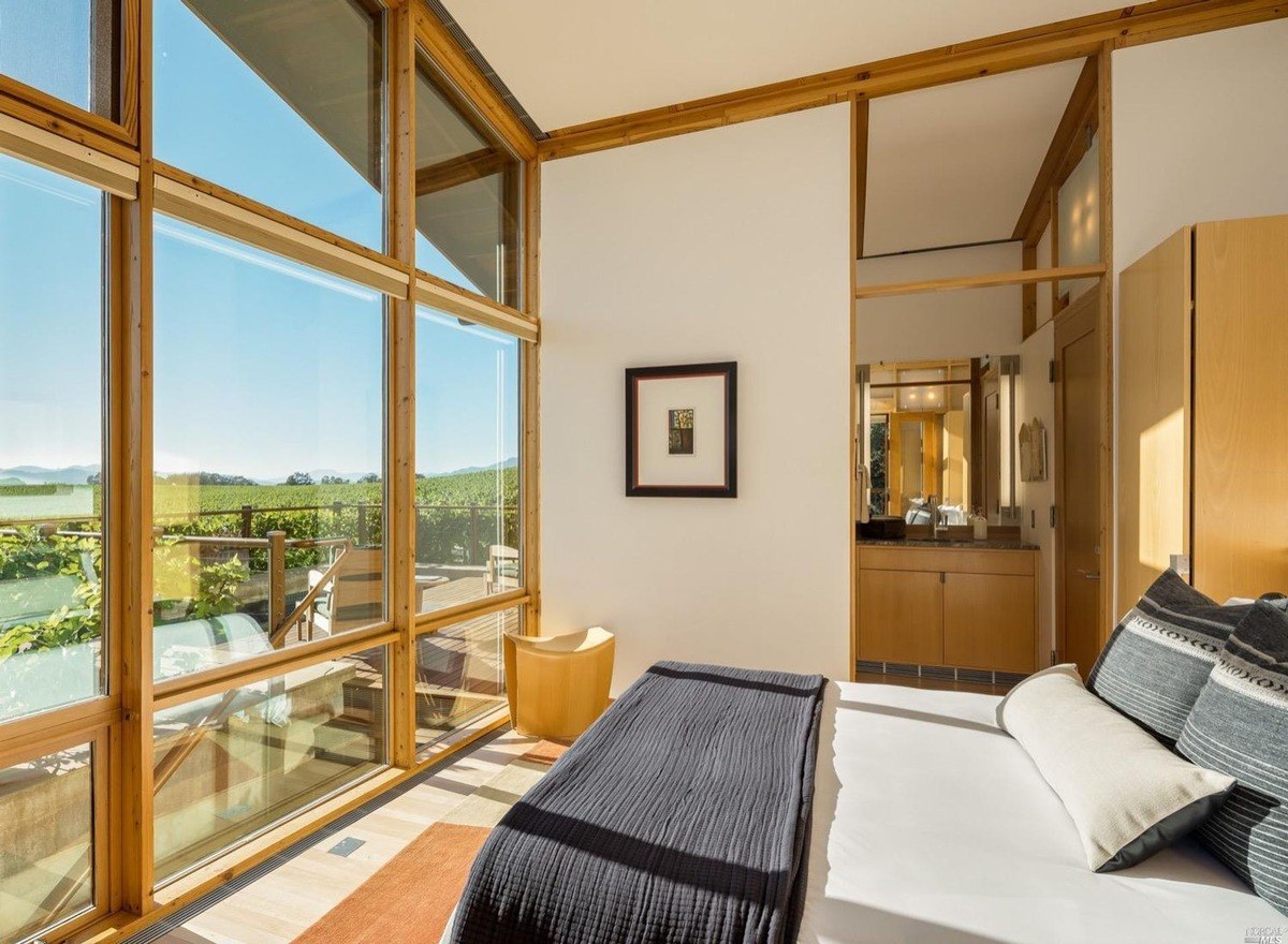 Bedroom space with expansive windows showcasing vineyards and an attached ensuite.