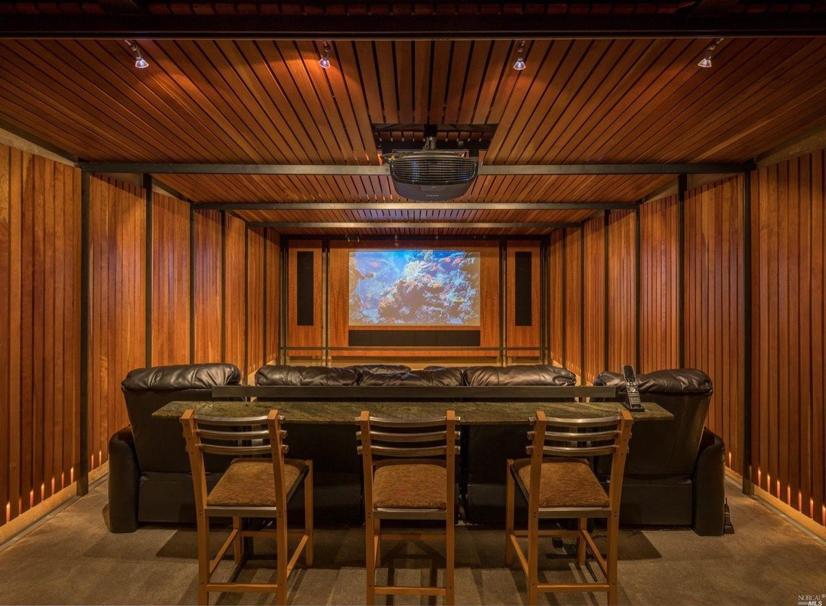 Home theater room lined with wooden paneling, a large projector screen, and comfortable leather seating.