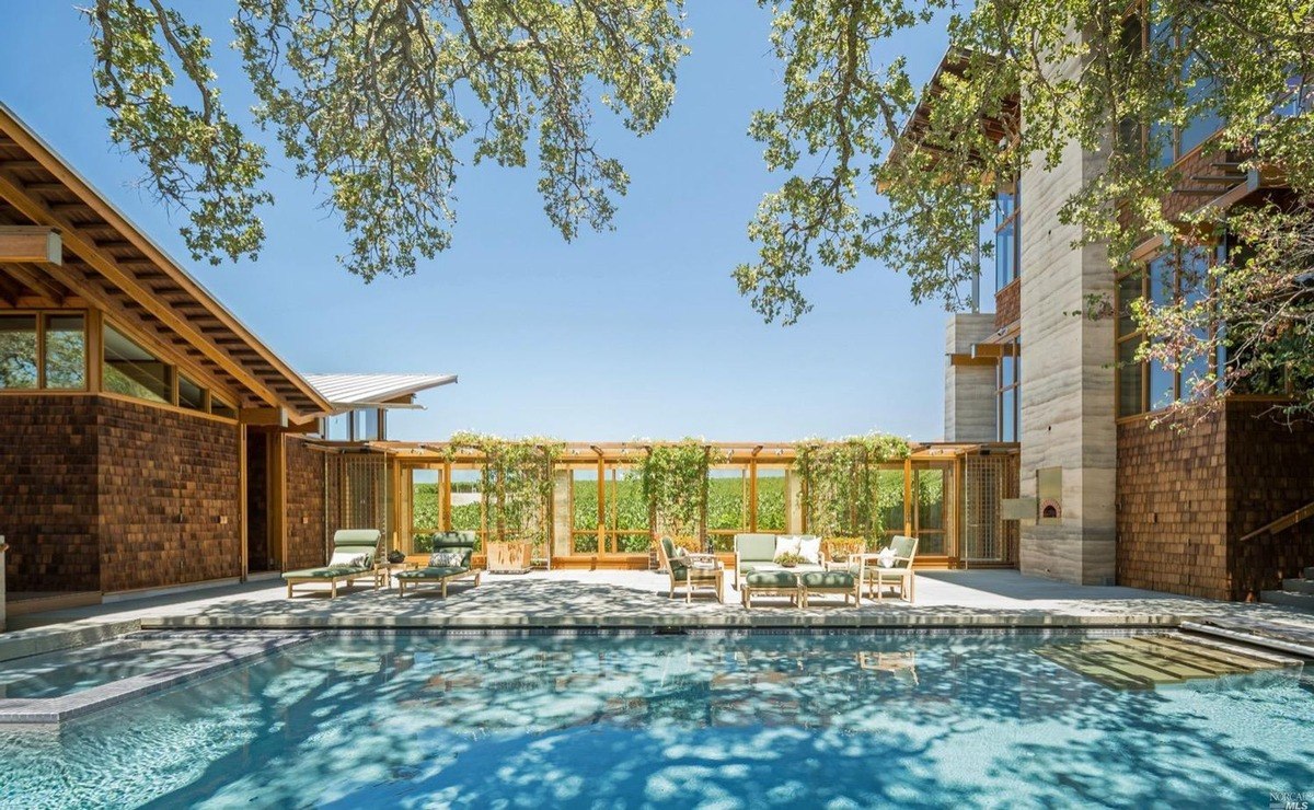 Poolside patio with shaded seating surrounded by greenery and modern architecture.