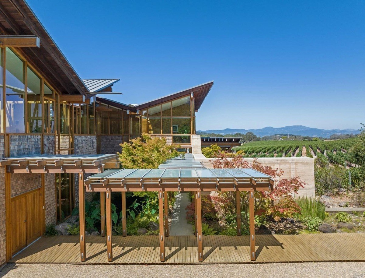 Outdoor walkway covered with a glass canopy, blending into the surrounding vineyard landscape and hills.