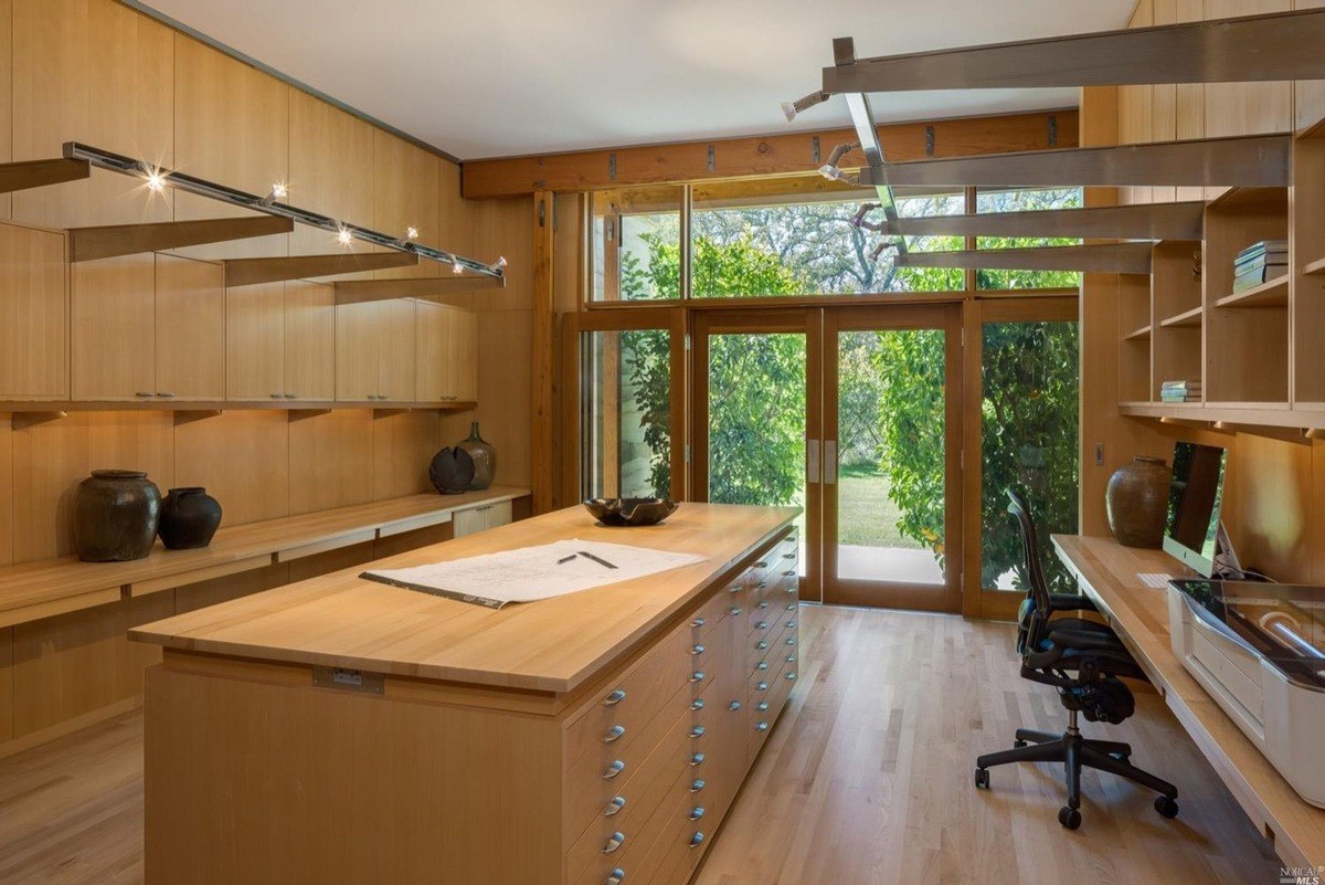 Home office showcases built-in shelving, a large center table, and garden-facing doors for natural light.