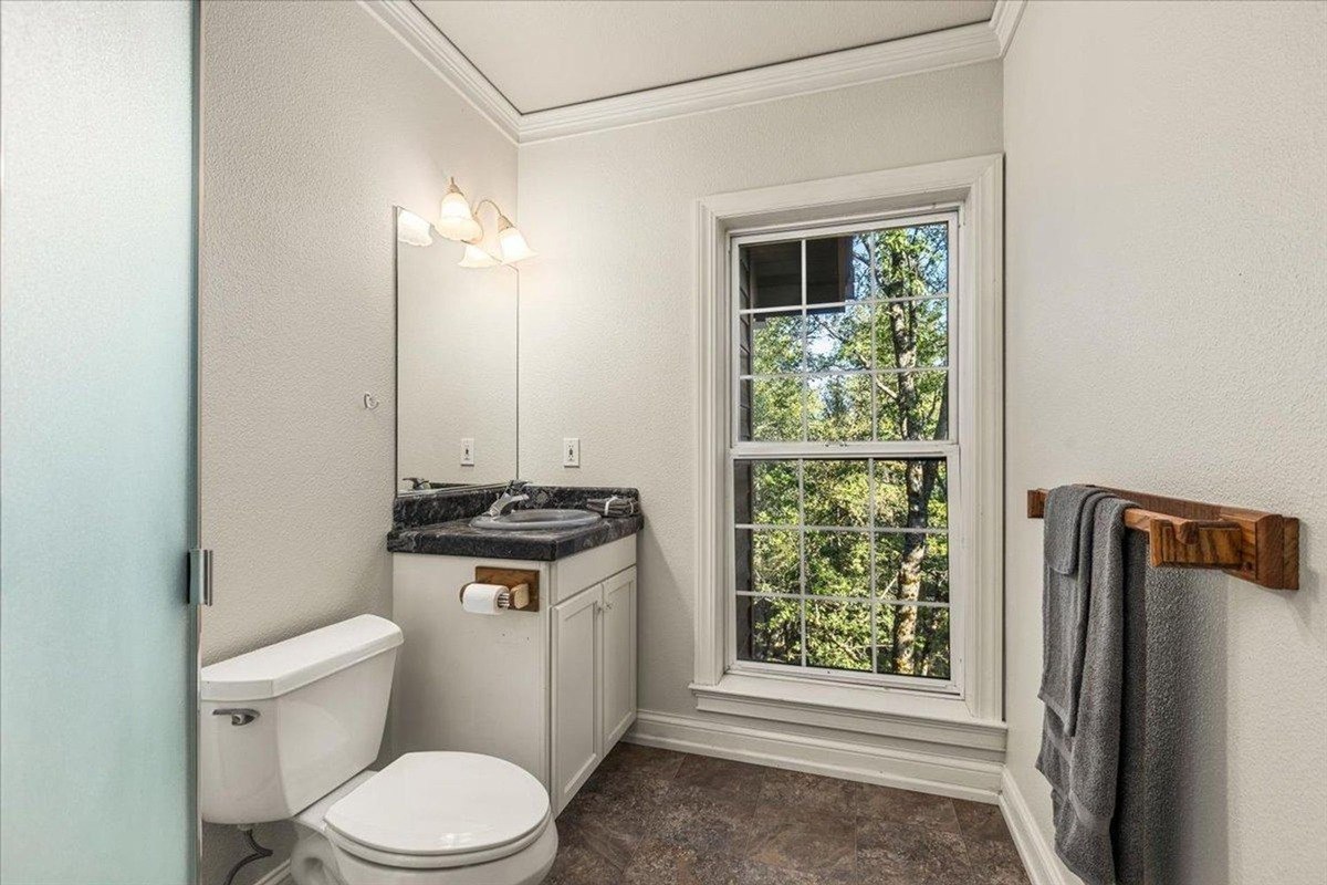 Minimalist bathroom with a granite countertop, white cabinetry, and a large window that frames outdoor views.