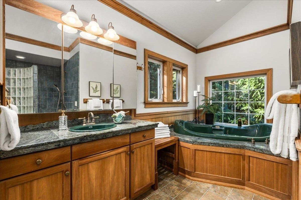 Luxurious bathroom with a green jetted tub, wood paneling, and dual sinks set beneath warm lighting.