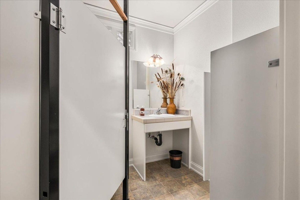 Powder room includes a single sink vanity, decorative wall-mounted mirrors, and a neutral-toned privacy partition.