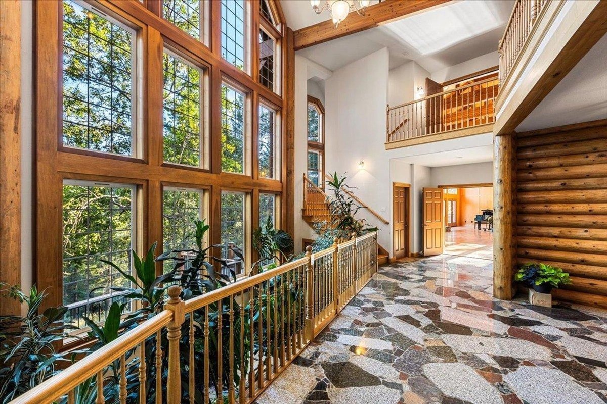 Bright foyer showcases double-height windows, polished stone flooring, and wooden railings that frame a scenic view.