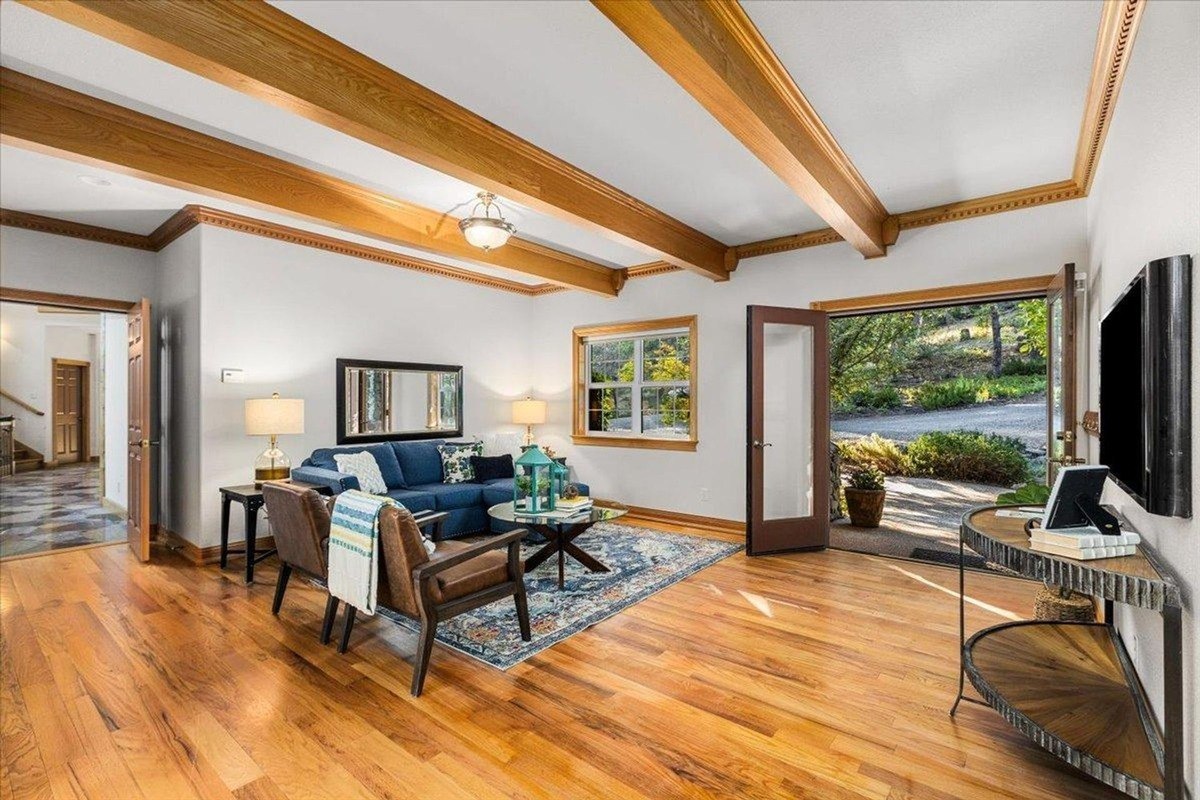 Living room boasts exposed wood beams, hardwood flooring, and an open layout with a cozy seating area.