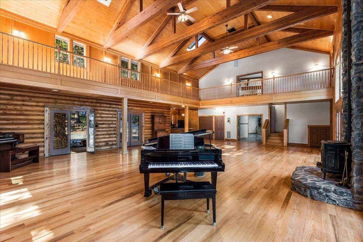 Expansive great room displays a grand piano and vaulted ceilings supported by wooden trusses, creating a lodge-like atmosphere.