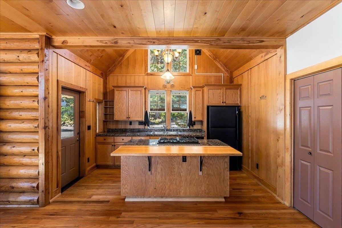 Rustic kitchen displays wood-paneled ceilings, cabinetry, and a central island with a gas stove.